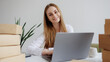© Sandu - Young woman working at a desk with a laptop surrounded by packages