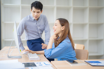 Fototapete - Two asian businesspeople are working together in the office, using a desktop computer to analyze data and discuss projects, showing teamwork and collaboration