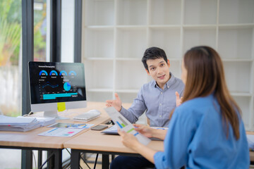 Poster - Two colleagues engage in a discussion, analyzing data displayed on a computer screen. Papers and graphs are spread across the desk, indicating a focus on business strategy and planning
