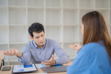 Aufkleber - Two Asian businesspeople discussing and explaining business profits while analyzing charts and graphs at an office desk during a productive morning meeting