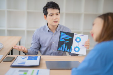 Aufkleber - Two Asian businesspeople discussing financial charts and graphs, analyzing performance and making strategic decisions in a bright, modern office environment
