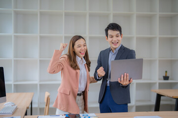 Poster - Two enthusiastic business professionals celebrating a successful achievement while looking at a laptop in a modern office setting. Shelves in the background suggest an organized workspace