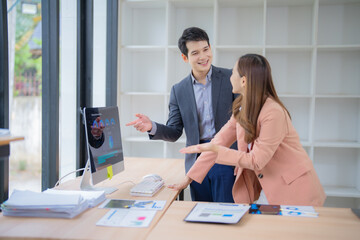 Poster - Two asian businesspeople discussing over financial charts showing data on computer screen in a modern office, they are analyzing financial data and planning new strategies