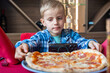 © Elena - Young Boy Watching Phone While Enjoying Pizza