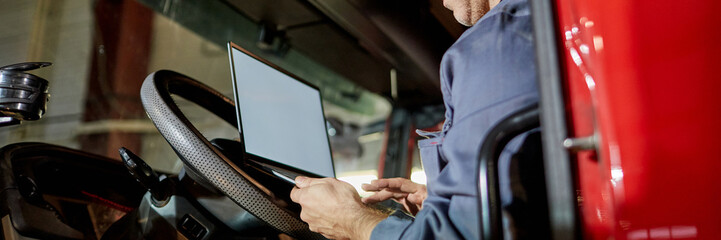 Close-up view of a person in a driver's seat using a laptop with focus on the steering wheel and computer screen