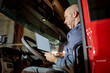 © Seventyfour - Professional truck driver using onboard technology in cab of red truck. Inside view of truck's cab with driver engaged in transportation-related task