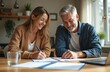 © Vadym - Relieved couple signs insurance forms in cozy home office. Smiling woman, gray-haired man review documents, planning future. Responsible financial decisions, security, peace of mind. Focus on middle