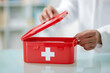 © Health Studio - A person opens a red first aid kit box on a table, preparing for medical emergencies.