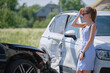 © bilanol - Stressed woman driver standing on street side shocked after car accident. Road safety and insurance concept