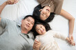 © winnievinzence - Top view of Asian family lying on bed and holding hands together. Little girl playing with parent on mattress. Love and family moment concept