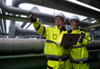 © Freeday photo - Workers in safety gear discuss project details while inspecting pipeline infrastructure in an industrial setting