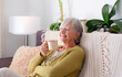 © luciano - Smiling Senior Woman Sitting Indoors in Cozy Sofa having a relaxing moments enjoying a cup of coffee. Elderly Lady and retirement lifestyle