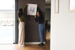 © Wavebreak Media - Positioning Diverse female friends hanging abstract art in living room, with sliding glass door