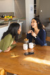 © Wavebreak Media - Laughing diverse female friends leaning at wooden table in open kitchen, with mugs and French press