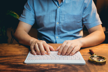 Poster - Person Typing on a Modern Keyboard While Sitting at a Wooden Table with a Magnifying Glass Nearby