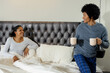 © Wavebreak Media - Couple sitting up on bed in modern bedroom, holding beige mugs and showcasing tufted headboard
