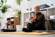 © Studio Marmellata - A woman in a headscarf sits on the floor, engrossed in her phone. She is surrounded by plants, a record player, and vinyl records, creating a cozy atmosphere for relaxation and digital connection.