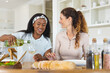 © Wavebreak Media - Diverse female friends pouring white wine at dining table in modern kitchen, with salad bowl