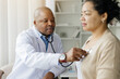 © Anastasiya - Mature doctor checking lungs of black female patient during medical checkup in clinic, friendly therapist man using stethoscope to examine breathing and heartbeat of young patient, closeup shot