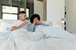 © Wavebreak Media - Sitting two men holding white mugs in bright modern bedroom, with light duvet and green foliage