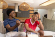 © Wavebreak Media - Showing diverse male friends reacting on sofa in modern living room, with popcorn bowl