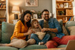 © La Famiglia - Happy family watching tv and eating popcorn on sofa at home