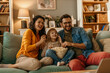 © La Famiglia - Happy family watching movie and eating popcorn on sofa