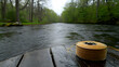 © Oktavia - Tranquil river landscape featuring fly fishing line spool resting on aged wood