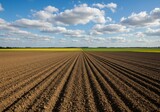 Farmland soil prepared for cultivation with blue sky and clouds in background