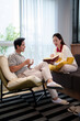 © Pichsakul - Asian Couple Relaxing at Home, Reading Book and Enjoying Coffee Together in Cozy Living Room with Natural Light and Modern Furniture