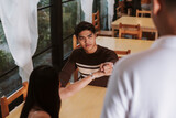 A frustrated Gen Z Southeast Asian man points to his watch while speaking to a waiter, expressing annoyance over long food wait times.