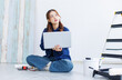 © Bangkok Click Studio - Asian young beautiful woman long curly hair wearing blue shirt jean sit on floor look at laptop computer learning before repairing room painting wall house or apartment rollers brush ladder background