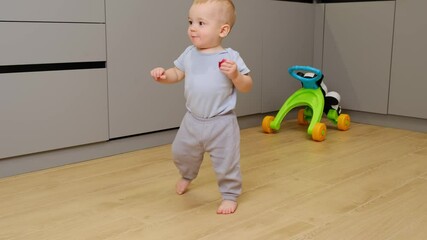 Happy exited baby boy learning to walk at home, while eat apple kitchen room. Cute little toddler taking his first steps without any help. Baby first steps and childhood concept