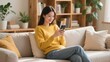 © meng - A woman in a yellow sweater using her smartphone on a couch
