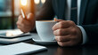 © thanakrit - Businessman in Suit Holding Coffee Cup at Desk with Stationery in Modern Office Environment