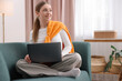 © New Africa - Smiling teenage girl with laptop on sofa at home