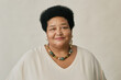 © Seventyfour - Portrait of mature African American woman with short curly hair wearing beaded necklace and white top, smiling softly at camera in studio