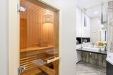 modern bathroom featuring a glass-doored sauna with wooden interior, contrasted by a sleek sink area with white cabinetry and hanging pendant lights