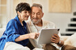 © LIGHTFIELD STUDIOS - Middle aged couple sharing laughter while using a tablet at home in cozy living room