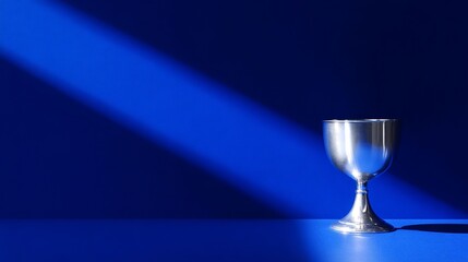 Poster - A gleaming silver cup stands on a smooth surface, illuminated by a striking blue light. The contrast creates an artistic and modern feel. This image is perfect for decoration and inspiration. AI