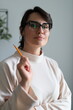 © Andrii Zastrozhnov - Caucasian young female with glasses holding pencil in light-colored sweater