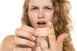 © vladimirfloyd - Woman looking frustrated, holding adhesive bandage with a focused expression. Blurred background suggesting minor injury or discomfort