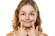 © vladimirfloyd - Young woman with wavy blonde hair forcing a smile by pushing her cheeks with fingers, demonstrating fake emotions against white background