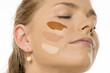 © vladimirfloyd - Close-up portrait of smiling young woman with different foundation shades swatched on her cheek, demonstrating makeup color matching process against white background
