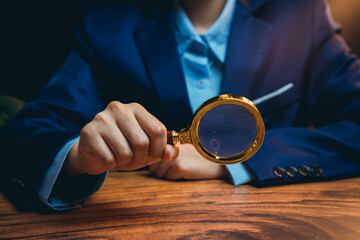 Poster - person holding golden magnifying glass while investigating subjects on wooden table in deep focus
