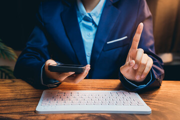 Poster - Business Professional in Suit Holding Phone Making Point with Finger while Sitting at Wooden Desk