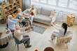 © Seventyfour - Group of elderly individuals participating in a seated exercise session inside comfortable living room with large windows and a walker nearby for support