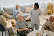 © Seventyfour - Nurse engaging with elderly residents at assisted living facility during activity time, promoting sense of community while seated at table