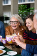© CarlosBarquero - Vertical. Group laughing mature people having snack sitting at cafe bar. Older friends toasting with coffee cups gathered together in terrace restaurant. Food and beverage lifestyle in senior citizens