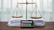 © Vanessa - A brass balance scale and a calculator sit on a stack of documents on a wooden desk, symbolizing law, justice, and finance. financial fairness, tax deal compliance